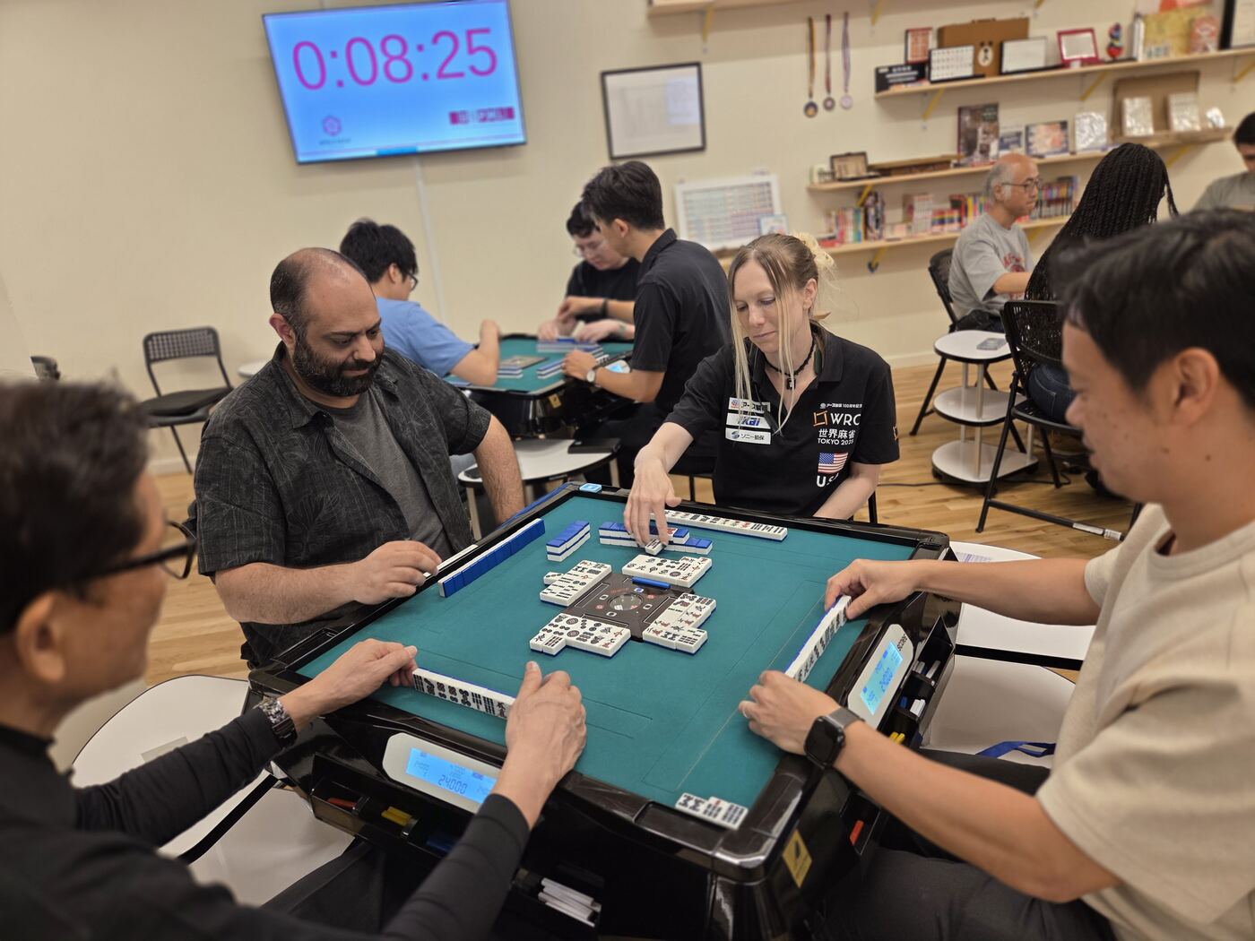 A player in a World Riichi Championship jersey mid-hand at an autotable