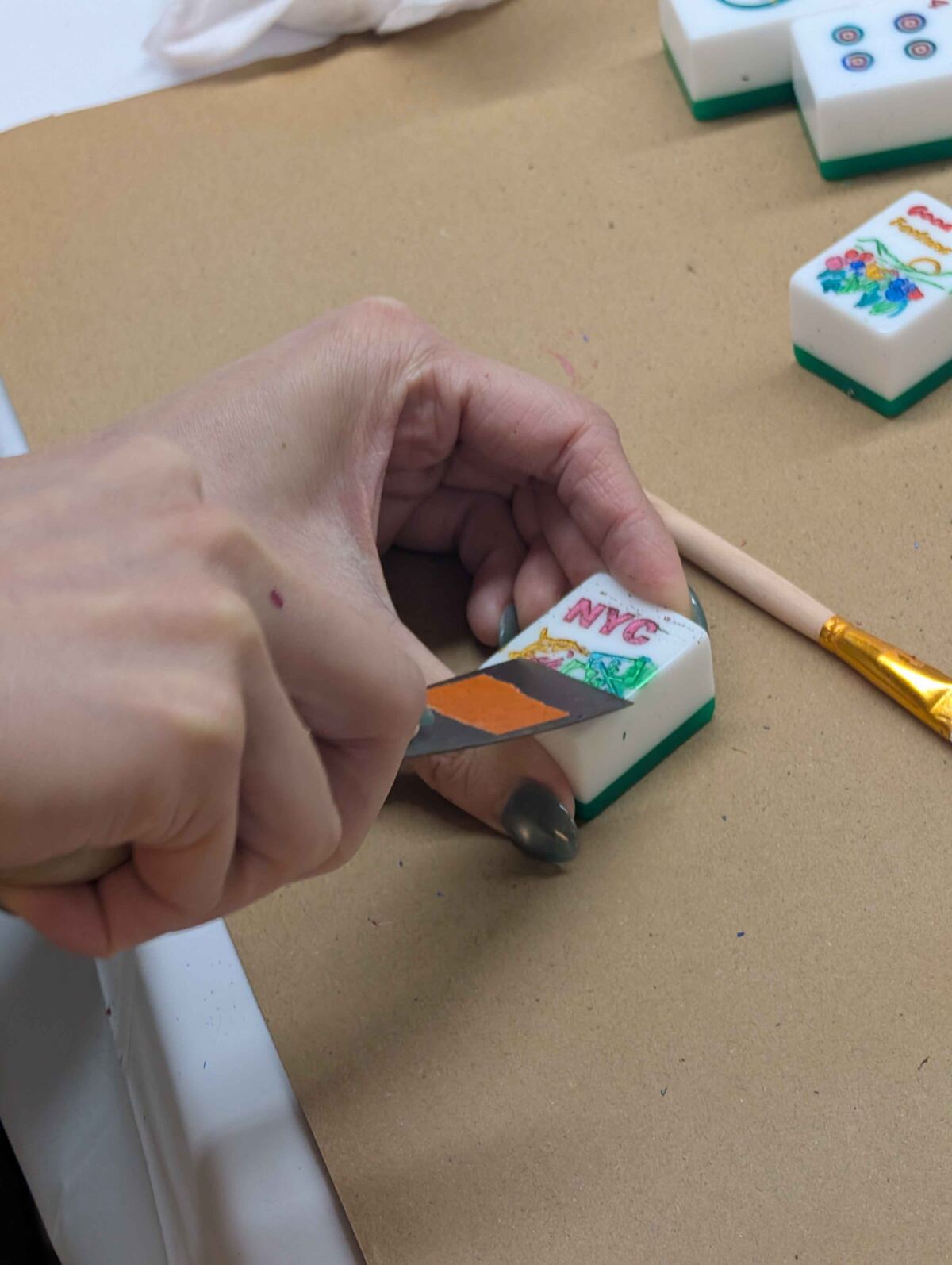Hands painting a custom NYC design onto a blank mahjong tile